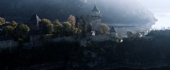 Movie still from “Medieval” (2022), directed by Petr Jákl – A castle on top of a hill with trees in the background; Extreme Wide shot, High angle