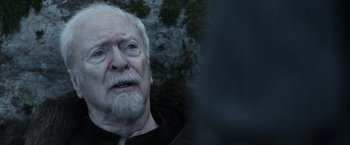 Movie still from “Medieval” (2022), directed by Petr Jákl – An old man with a beard is looking into the distance; Close Up shot, Over the shoulder angle