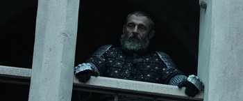 Movie still from “Medieval” (2022), directed by Petr Jákl – A man with a beard wearing a suit of armor; Medium shot, Low angle