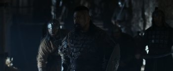 Movie still from “Medieval” (2022), directed by Petr Jákl – A man with a beard wearing armor and holding a shield; Medium shot, Over the shoulder angle