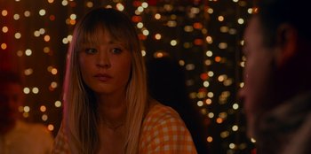 Movie still from “Meet Cute” (2022), directed by Alex Lehmann – A woman with blonde hair is standing in front of a string of lights; Close Up shot, Over the shoulder angle