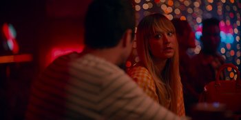 Movie still from “Meet Cute” (2022), directed by Alex Lehmann – A man and a woman sitting at a table in front of each other in front of lights; Close Up shot, Over the shoulder angle
