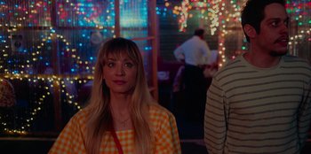 Movie still from “Meet Cute” (2022), directed by Alex Lehmann – A woman standing in front of a crowd of people at a party; Medium shot, Over the shoulder angle