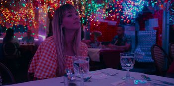 Movie still from “Meet Cute” (2022), directed by Alex Lehmann – A woman sitting at a table with a glass of water; Medium shot, Over the shoulder angle