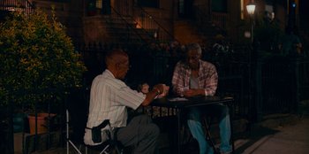 Movie still from “Meet Cute” (2022), directed by Alex Lehmann – Two older men sitting at a table playing cards; Wide shot, High angle