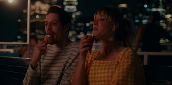 Movie still from “Meet Cute” (2022), directed by Alex Lehmann – A man and a woman are eating a donut; Medium shot, High angle
