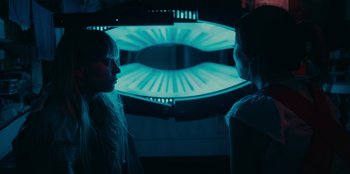 Movie still from “Meet Cute” (2022), directed by Alex Lehmann – Two women standing next to each other in front of an illuminated screen; Close Up shot, Over the shoulder angle