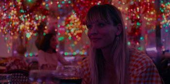Movie still from “Meet Cute” (2022), directed by Alex Lehmann – A woman sitting at a table in front of a bunch of lights; Close Up shot, Over the shoulder angle