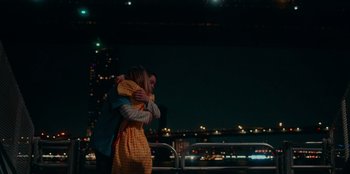 Movie still from “Meet Cute” (2022), directed by Alex Lehmann – A man and a woman hugging in front of a city skyline at night; Medium shot, High angle