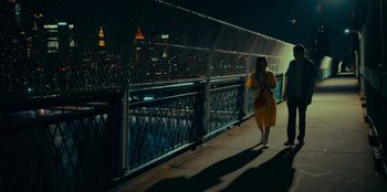 Movie still from “Meet Cute” (2022), directed by Alex Lehmann – A woman in a yellow dress walking on a bridge; Extreme Wide shot, High angle