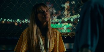 Movie still from “Meet Cute” (2022), directed by Alex Lehmann – A woman standing in front of a chain link fence at night; Close Up shot, Over the shoulder angle