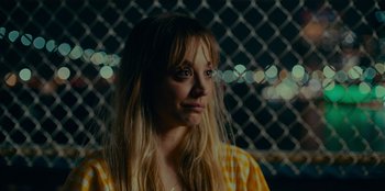 Movie still from “Meet Cute” (2022), directed by Alex Lehmann – A woman with blonde hair is standing in front of a chain link fence at night; Close Up shot, Over the shoulder angle