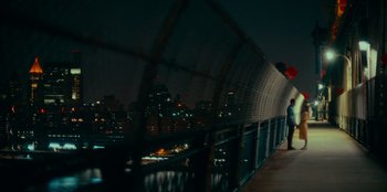 Movie still from “Meet Cute” (2022), directed by Alex Lehmann – A person standing on a bridge at night with a city in the background; Extreme Wide shot, High angle