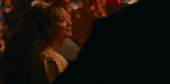 Movie still from “Meet Cute” (2022), directed by Alex Lehmann – A woman in a yellow and white checkered dress is smiling; Close Up shot, Over the shoulder angle