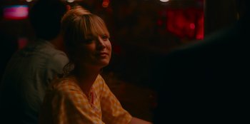 Movie still from “Meet Cute” (2022), directed by Alex Lehmann – A woman in a yellow and white checkered shirt is smiling; Close Up shot, Over the shoulder angle