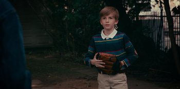 Movie still from “Meet Cute” (2022), directed by Alex Lehmann – A young boy holding a baseball glove in his hands; Medium shot, Over the shoulder angle