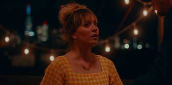 Movie still from “Meet Cute” (2022), directed by Alex Lehmann – A woman in an orange checkered dress looking to her left; Close Up shot, Over the shoulder angle
