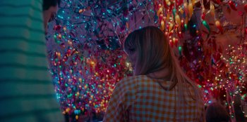 Movie still from “Meet Cute” (2022), directed by Alex Lehmann – A woman standing in front of a bunch of christmas lights; Medium shot, High angle