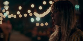 Movie still from “Meet Cute” (2022), directed by Alex Lehmann – A woman with long blonde hair standing in front of lights at night; Close Up shot, Over the shoulder angle