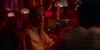 Movie still from “Meet Cute” (2022), directed by Alex Lehmann – A woman sitting at a table in front of lights; Close Up shot, Over the shoulder angle