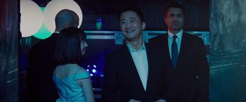 Movie still from “Meg 2: The Trench” (2023), directed by Ben Wheatley – A man in a suit and tie standing next to a woman in a white dress; Medium shot, Over the shoulder angle