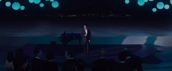 Movie still from “Meg 2: The Trench” (2023), directed by Ben Wheatley – A man standing on a stage in front of an audience at night; Extreme Wide shot, High angle