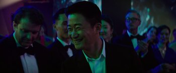 Movie still from “Meg 2: The Trench” (2023), directed by Ben Wheatley – A man in a suit smiling at a party; Close Up shot, Over the shoulder angle