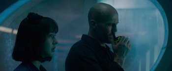 Movie still from “Meg 2: The Trench” (2023), directed by Ben Wheatley – A man with a beard is talking on a cell phone while a woman looks on; Close Up shot, Over the shoulder angle