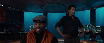 Movie still from “Meg 2: The Trench” (2023), directed by Ben Wheatley – A man in a hat and glasses is in front of another man in an underwater scene; Medium shot, Over the shoulder angle
