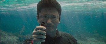 Movie still from “Meg 2: The Trench” (2023), directed by Ben Wheatley – A man holding up a cell phone in front of an underwater scene; Close Up shot, High angle