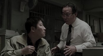 Movie still from “Memories of Murder” (2003), directed by Bong Joon Ho – Two men are talking to each other in a jail cell; Medium shot, Low angle