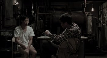 Movie still from “Memories of Murder” (2003), directed by Bong Joon Ho – Two men sitting at a table in a room; Medium shot, High angle