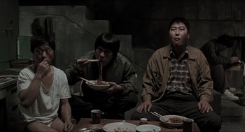 Movie still from “Memories of Murder” (2003), directed by Bong Joon Ho – A group of people sitting around a table eating food; Medium shot, High angle