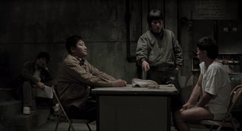 Movie still from “Memories of Murder” (2003), directed by Bong Joon Ho – Two men sitting at a table in front of one another; Wide shot, High angle