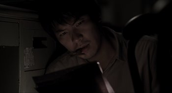 Movie still from “Memories of Murder” (2003), directed by Bong Joon Ho – A man sitting in front of a laptop computer in a dark room; Close Up shot, High angle