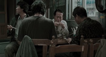 Movie still from “Memories of Murder” (2003), directed by Bong Joon Ho – A group of people sitting around a table eating; Medium shot, Over the shoulder angle
