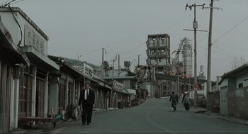 Movie still from “Memories of Murder” (2003), directed by Bong Joon Ho – A man in a suit and tie walking down a street; Extreme Wide shot, Low angle