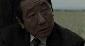 Movie still from “Memories of Murder” (2003), directed by Bong Joon Ho – An older asian man in a suit and tie; Close Up shot, Over the shoulder angle