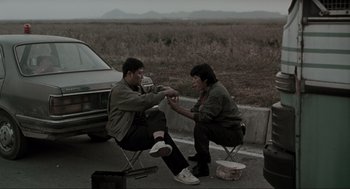 Movie still from “Memories of Murder” (2003), directed by Bong Joon Ho – Two men sitting on a road next to each other; Wide shot, High angle