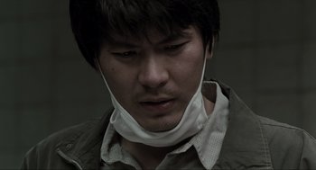 Movie still from “Memories of Murder” (2003), directed by Bong Joon Ho – A man wearing a face mask looking down at his face; Close Up shot, Low angle