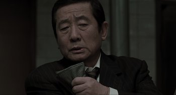 Movie still from “Memories of Murder” (2003), directed by Bong Joon Ho – An older man in a suit and tie holding a wallet; Close Up shot, Over the shoulder angle