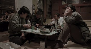 Movie still from “Memories of Murder” (2003), directed by Bong Joon Ho – A group of people sitting around a table eating food; Wide shot, High angle