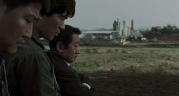 Movie still from “Memories of Murder” (2003), directed by Bong Joon Ho – Two men are standing next to each other in a field; Medium shot, Over the shoulder angle