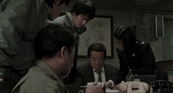 Movie still from “Memories of Murder” (2003), directed by Bong Joon Ho – A group of people gathered around an older man; Medium shot, High angle