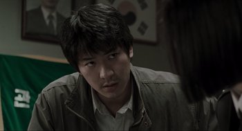 Movie still from “Memories of Murder” (2003), directed by Bong Joon Ho – A man with a black jacket is looking at the camera; Close Up shot, Over the shoulder angle
