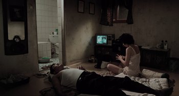 Movie still from “Memories of Murder” (2003), directed by Bong Joon Ho – A man and a woman sitting on the floor watching television; Wide shot, High angle