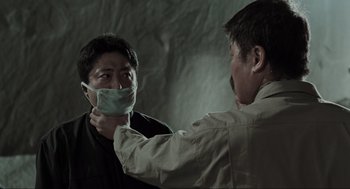 Movie still from “Memories of Murder” (2003), directed by Bong Joon Ho – A man is putting a face mask on another man's face; Close Up shot, Over the shoulder angle
