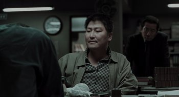 Movie still from “Memories of Murder” (2003), directed by Bong Joon Ho – A man sitting at a table with his eyes closed; Close Up shot, Over the shoulder angle