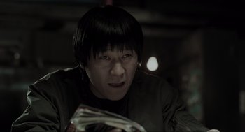 Movie still from “Memories of Murder” (2003), directed by Bong Joon Ho – A man is looking at the camera while holding a newspaper; Close Up shot, Low angle