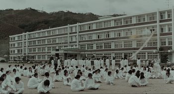 Movie still from “Memories of Murder” (2003), directed by Bong Joon Ho – A group of people sitting on the ground in front of a building; Extreme Wide shot, High angle